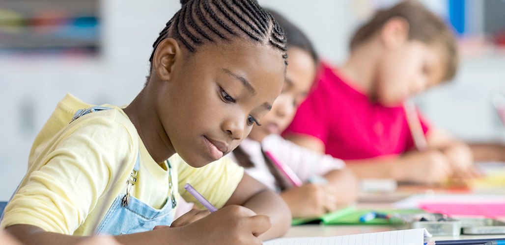 10 jarig meisje doet haar huiswerk in de klas, op achtergrond nog 2 kinderen die hetzelfde doen | Actueelbericht: Er waren nooit eerder zorgen om dit kind...