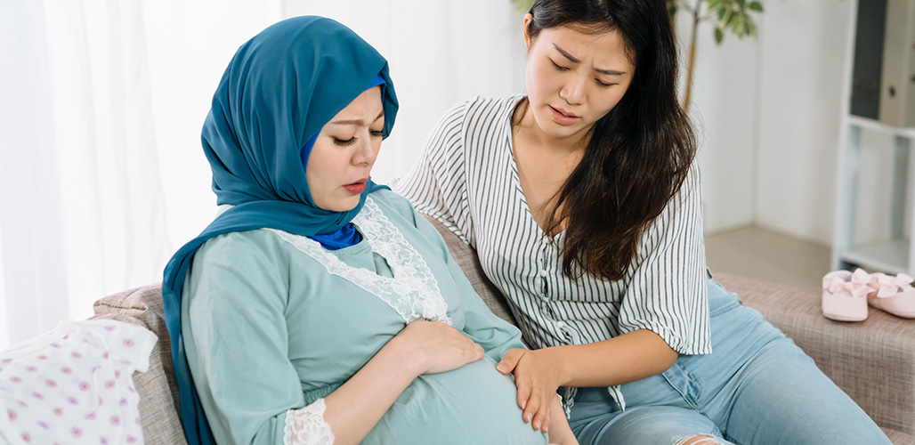 Een vriendin op bezoek bij een zwangere jongedame, voelen samen aan de buik om de baby te voelen | Actueelbericht: Waarom informele steun juist voor prille ouders zo belangrijk is