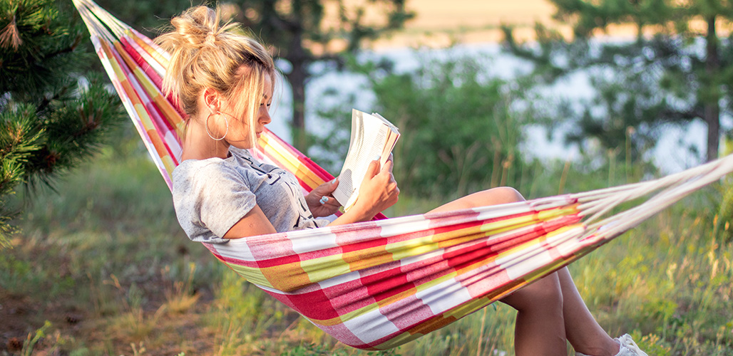 Jongedame op vakantie in hangmat in de tuin met boek | Actueelbericht: 10x lezen over mentaal welzijn
