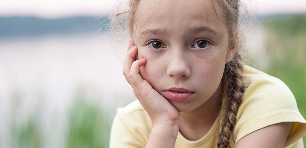 Meisje kijkt vanaf strand indringend in de camera, alsof ze een geheim heeft. | Actueelbericht: Wat doe je als een kind je vertelt dat het thuis geslagen wordt?