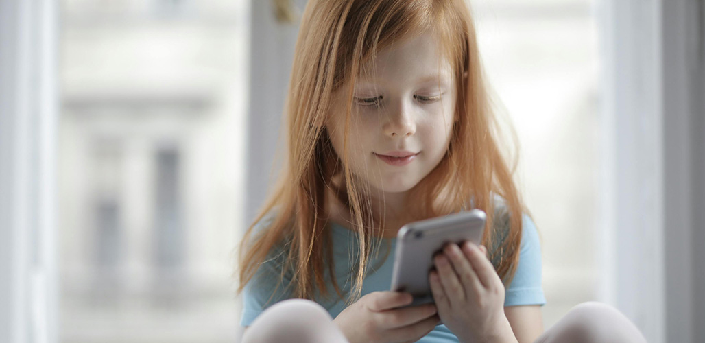 Roodharig  meisje zit voor het raam en kijkt naar het scherm van een mobiele telefoon  | Actueelbericht: Nieuw! OpPepper App