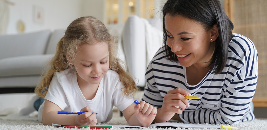 pleegouder ligt samen met meisje op de grond te kleuren
