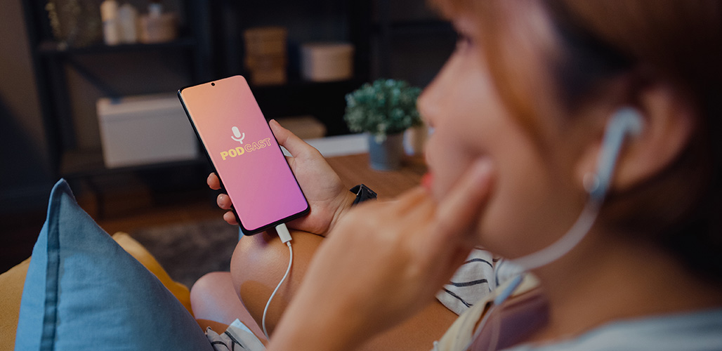 Vrouw luistert op de bank aandachtig naar podcast via haar telefoon | Actueelbericht: 7 Podcast-tips met verhalen en inzichten over jeugd en gezinnen