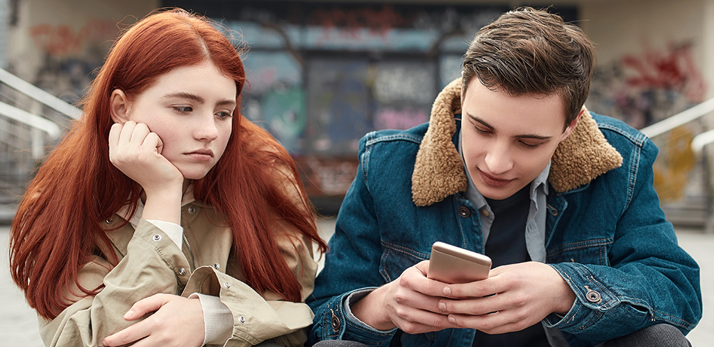 Meisje kijkt verveeld terwijl haar vriendje op zijn telefoon zit en haar volledig negeert. | Actueelbericht: Eerste resultaten Nederlands onderzoek naar datinggeweld onder jongeren bekend