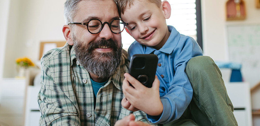 Vader en zoon bekijken samen iets online op vader's mobiele telefoon | Actueelbericht: Wat iedere professional zou moeten weten over online (on)veiligheid