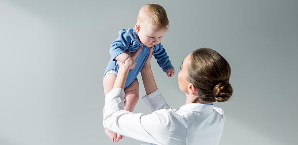 Arts houdt een vrolijk ogende baby omhoog | Actueelbericht: Webinar – Een baby met een blauwe plek, dat is gek 
