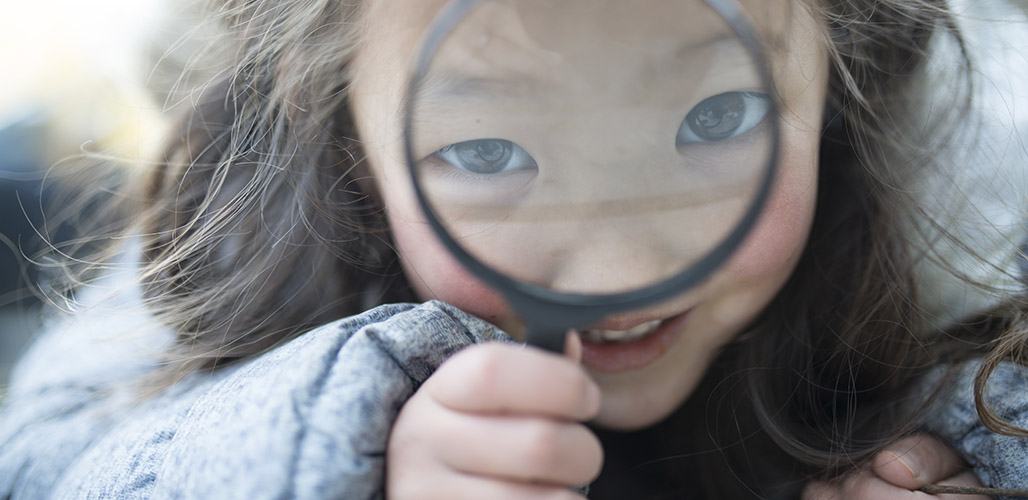 Meisje kijkt door vergrootglas in camera