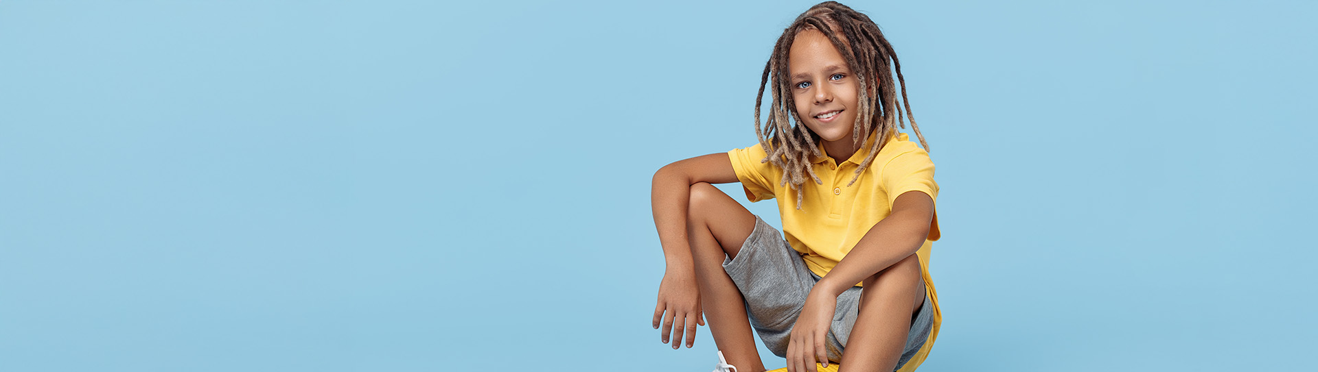 Augeo OpPepper App | Jongen met dreads zit op een skateboard. Draagt geel short met korte mouwen en korte broek.