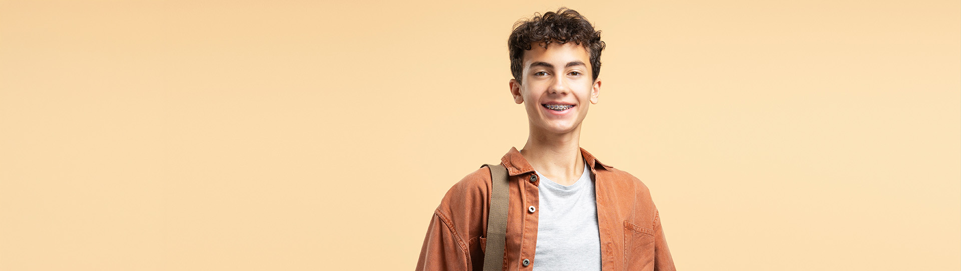 Jongen met beugel kijkt glimlachend in camera.