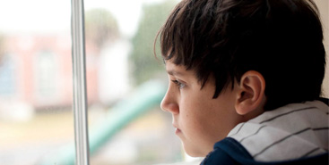 Jongen kijkt bezorgd uit het raam. Misschien geen zin in de zomervakantie??