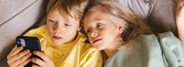 2 jonge kinderen kijken liggend op de bank naar 1 mobiele telefoon