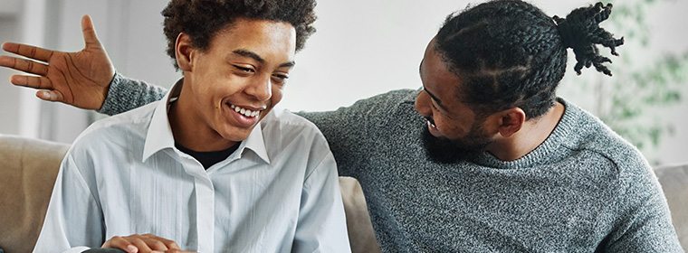 Mentaal welzijn en jongeren | Zoon lacht na opmerking vader die arm om hem heen heeft en trots naar zoon kijkt