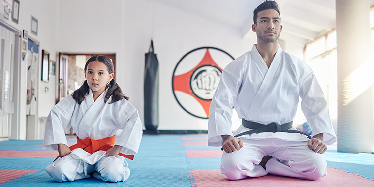 Sensei en leerling zitten geduldig op knieen in dojo te wachten.