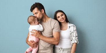 Ouderschap - Vader zoent baby op voorhoofd. Moeder kijkt gelukkig